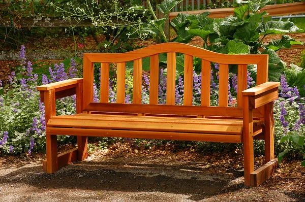Solid wood garden bench with armrests, classic design, placed in a flower-filled outdoor space – perfect outdoor seating for patios or parks.